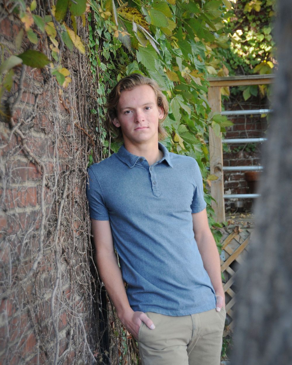 Casual portrait against brick wall with ivy wearing blue polo shirt.
