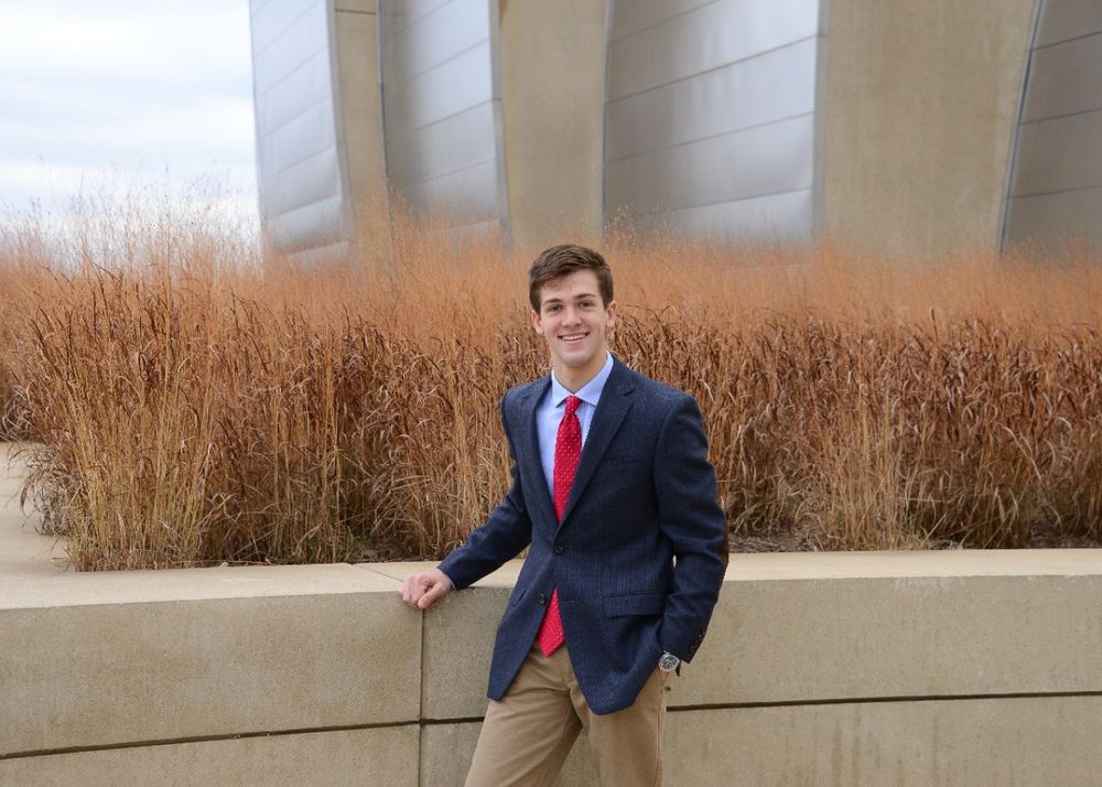 Professional portrait of suit-clad person against modern building with ornamental grasses.