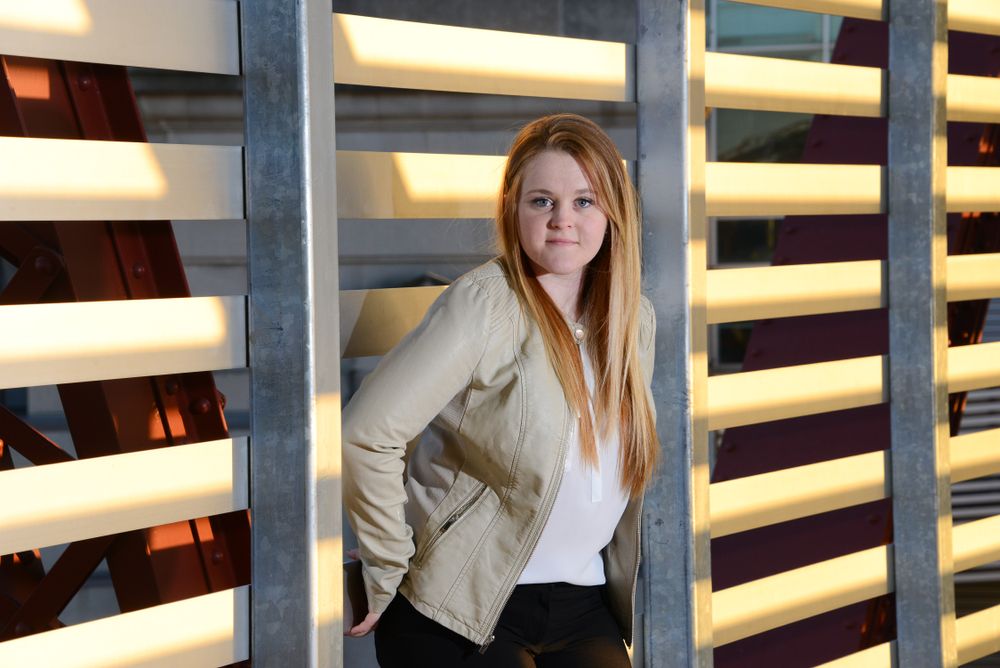 Professional woman in business attire posed against modern slatted wall with dramatic lighting.