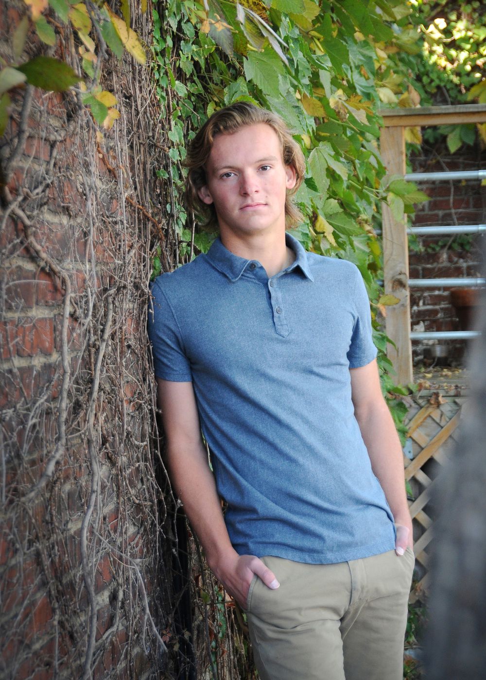 Portrait against brick and ivy wall wearing blue polo shirt and khaki pants.