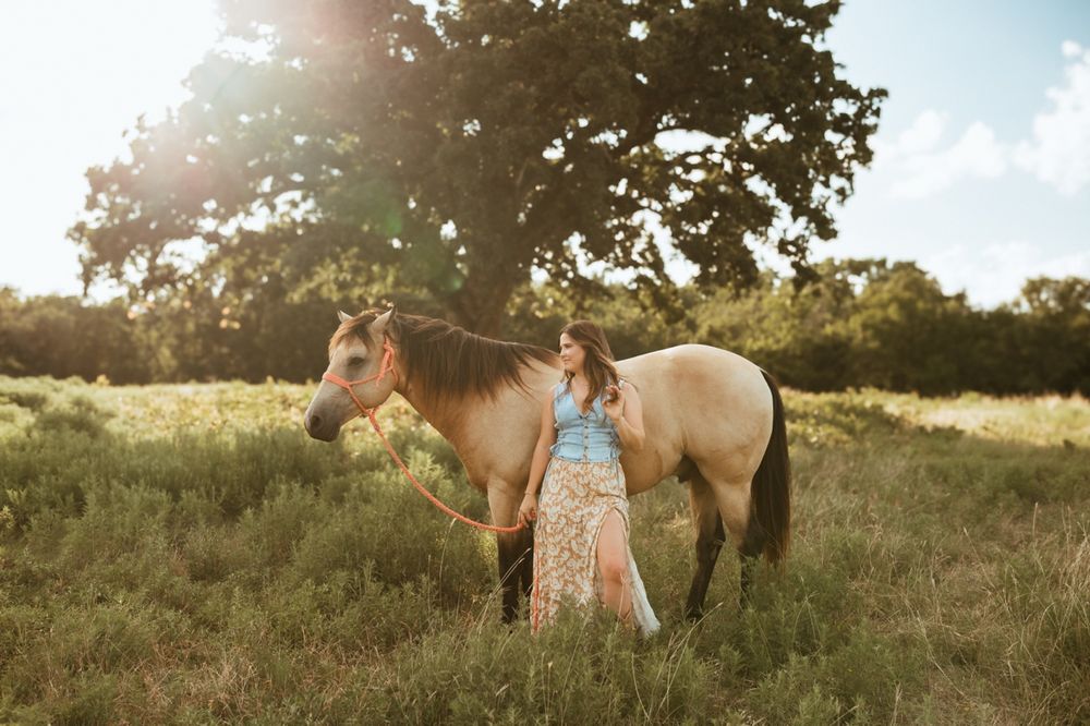 Family poses with two horses in a sunlit meadow at golden hour during a sunset photo session.