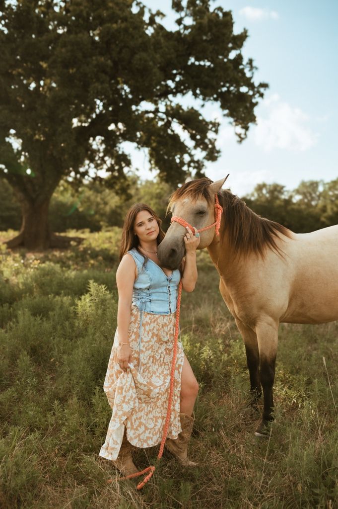 Little girl in a dress spending time outdoors with a brown horse on a sunny summer afternoon.