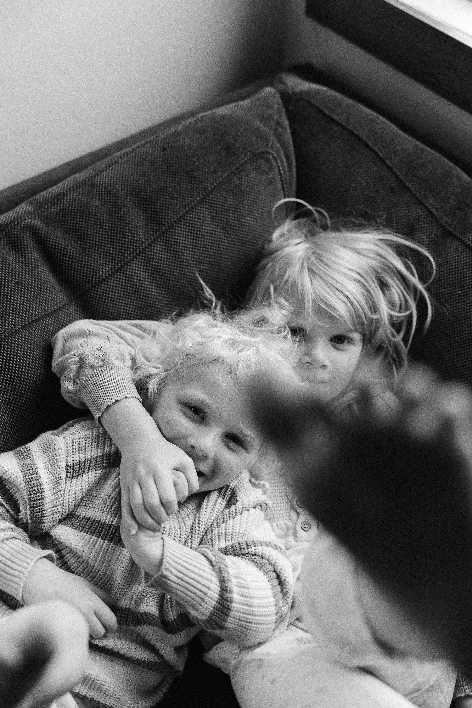 Black and white photograph showing two small children resting on a plush couch together.