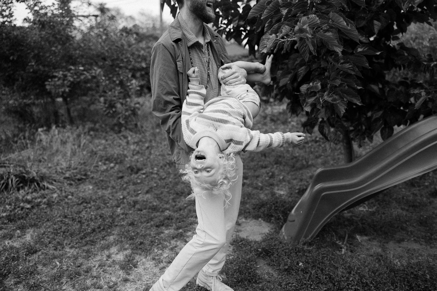 Black and white photo of a toddler being held up playfully in a garden setting.