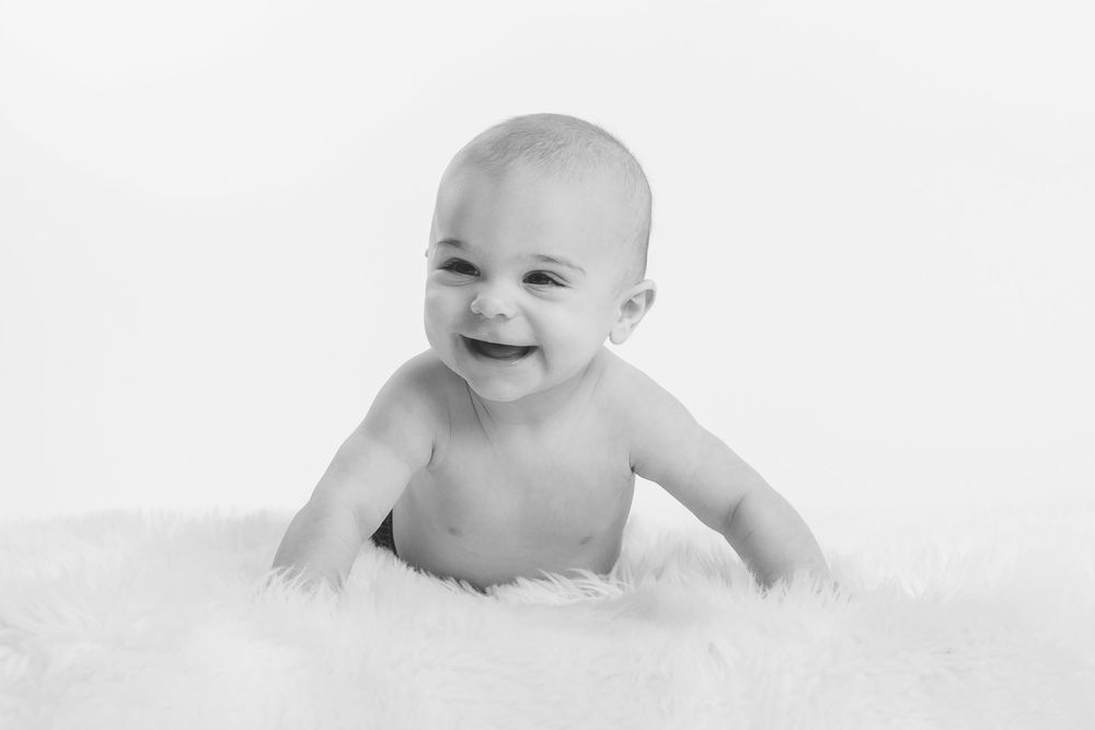 A smiling baby lies on soft white fur in a black and white portrait.