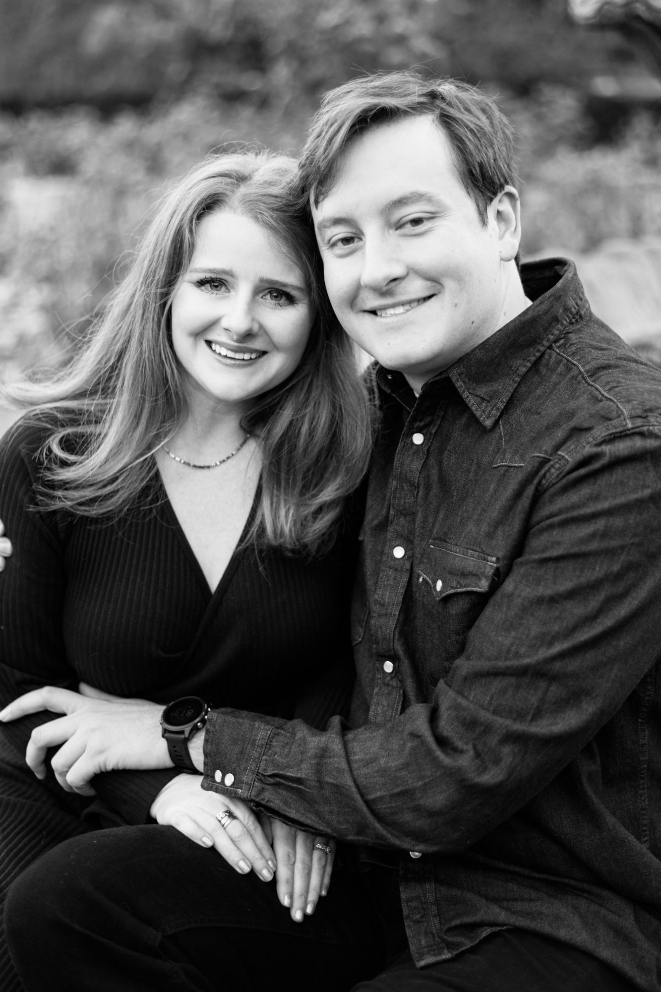 A romantic black and white portrait of a couple smiling together outdoors.