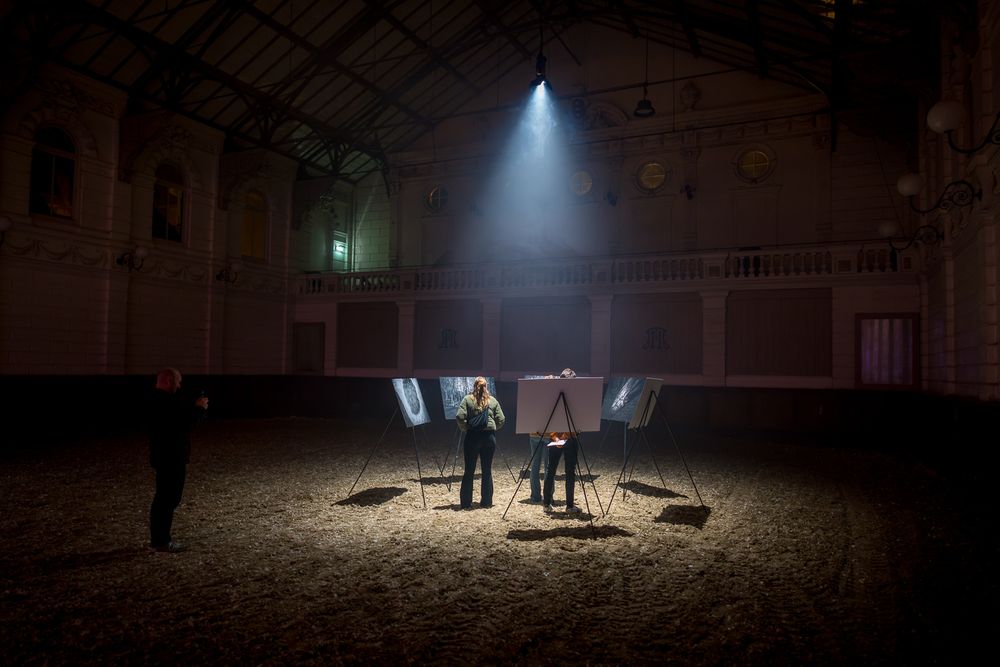 Performance art installation in dimly lit historic venue with dramatic spotlight beams.