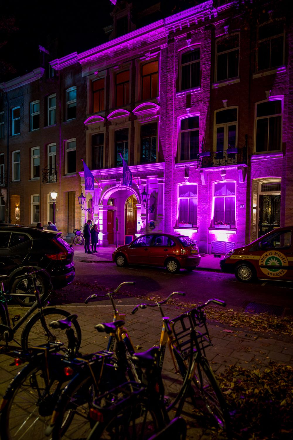 Historic building illuminated with vibrant purple lighting at night with bicycles parked in the foreground.