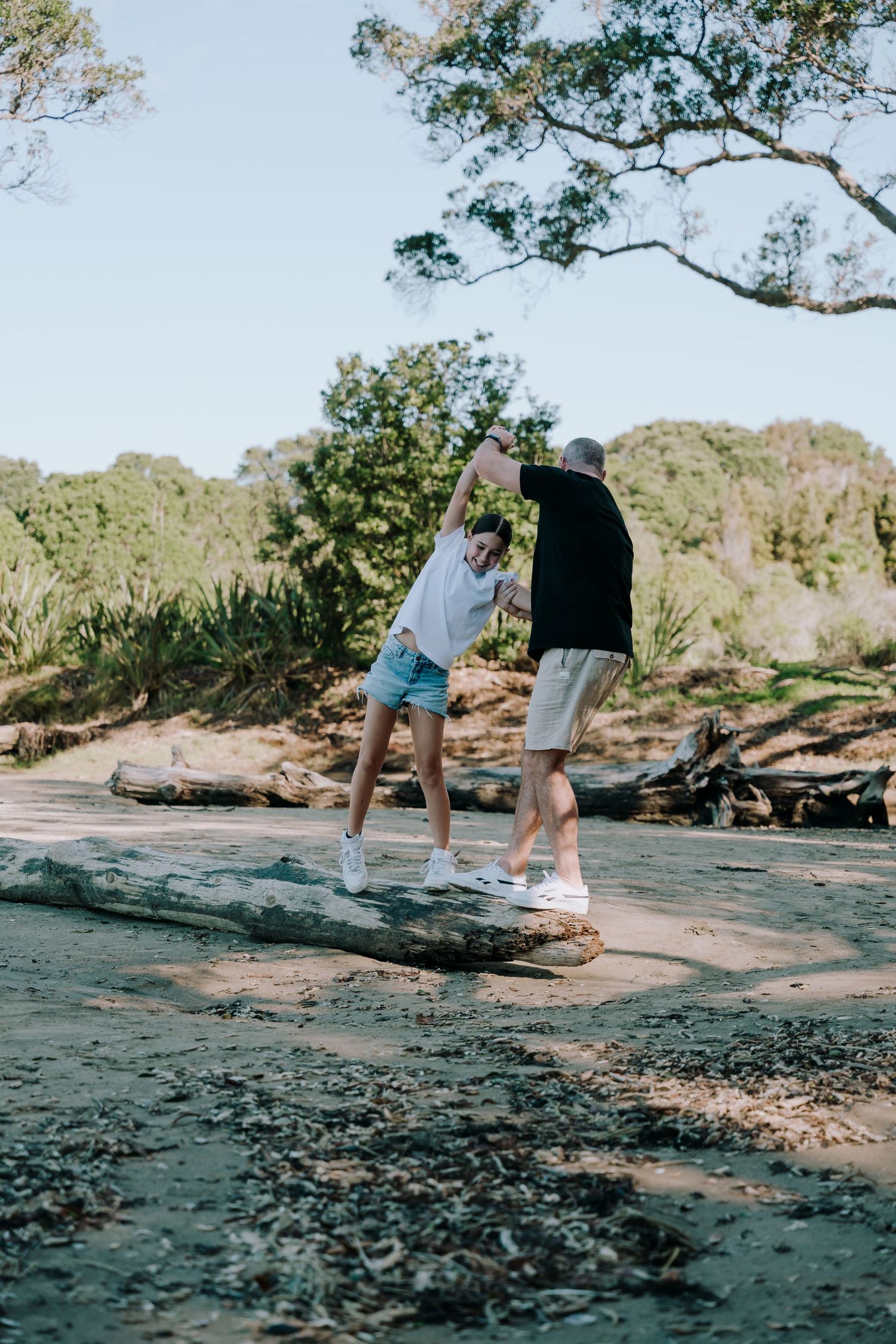 Two people holding hands while balancing on rocks by the water's edge in a scenic natural setting.