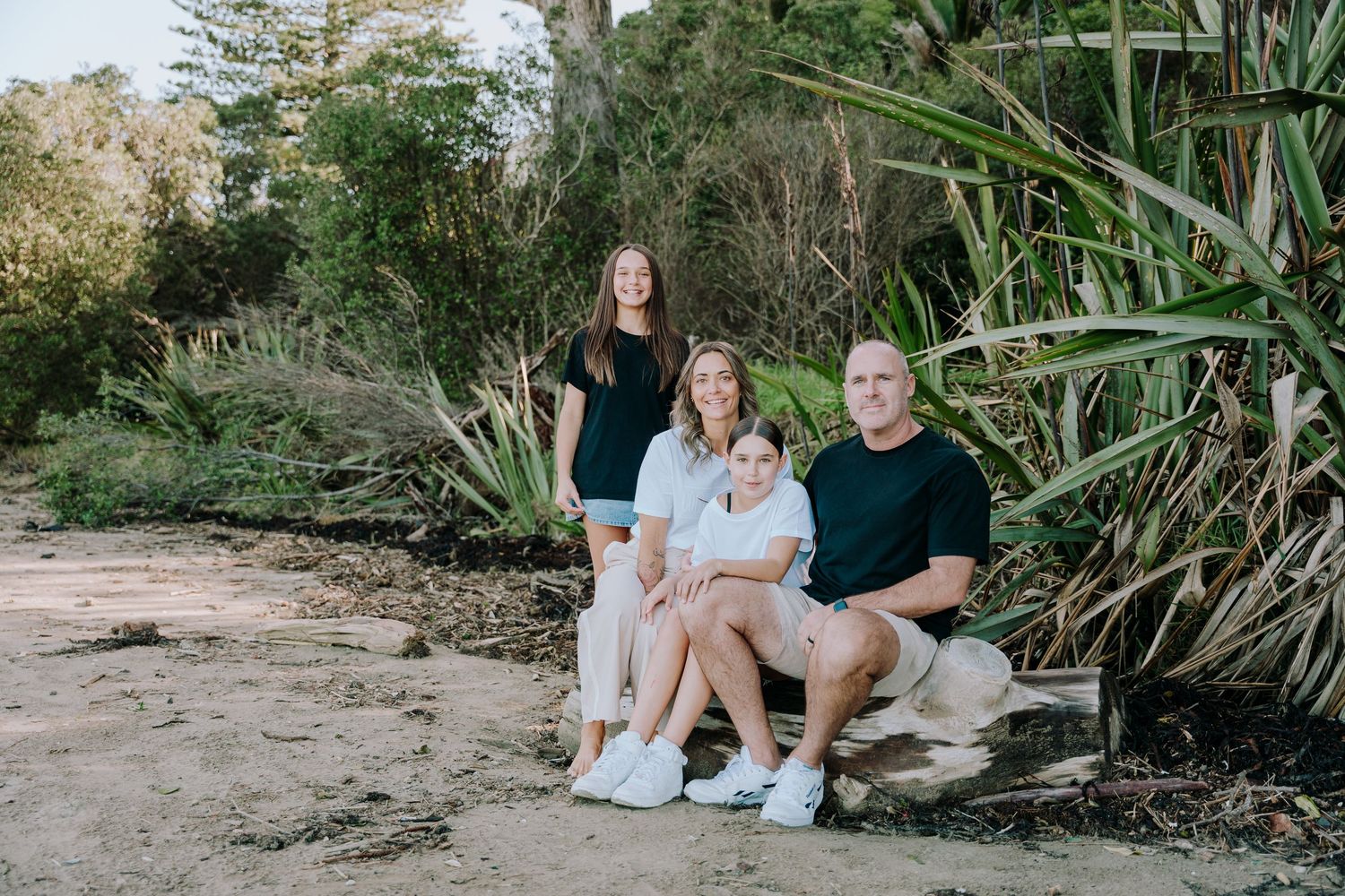 Three people sit together on a sandy path surrounded by lush tropical plants and greenery.
