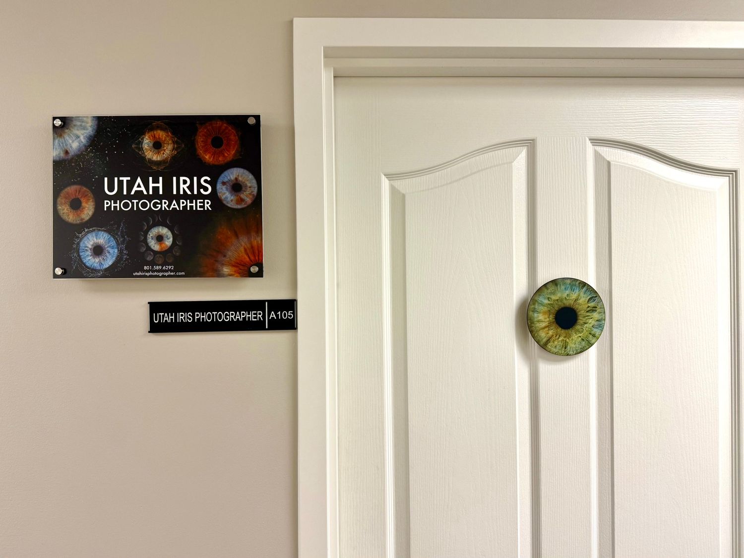 A white door with a green eyeball decoration next to a Utah Iris sign mounted on the wall.