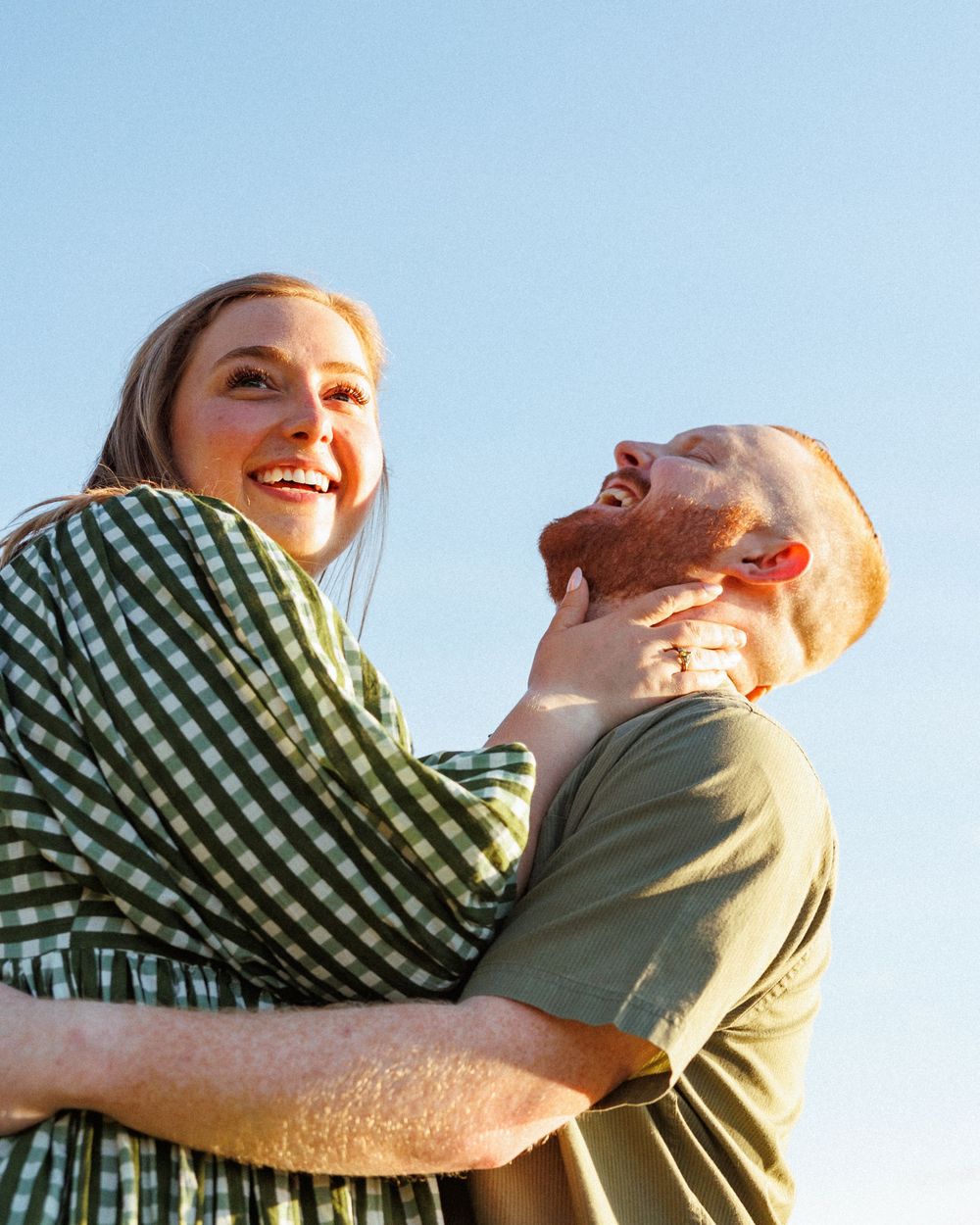 A couple sharing joyful embraces outdoors against a bright blue sky background.