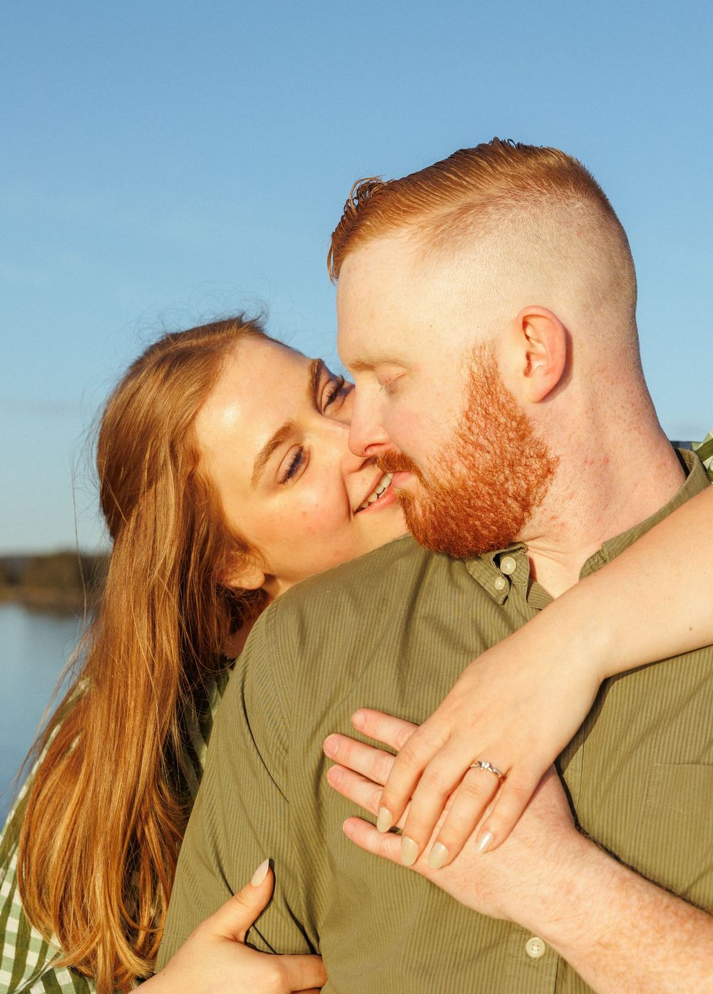A couple shares a tender romantic moment at sunset, with sun-lit hair and a natural outdoor setting.