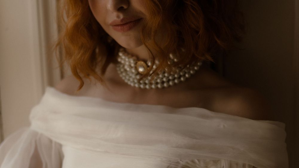 Close-up portrait of someone wearing a pearl choker necklace and off-shoulder white tulle gown in soft natural light.