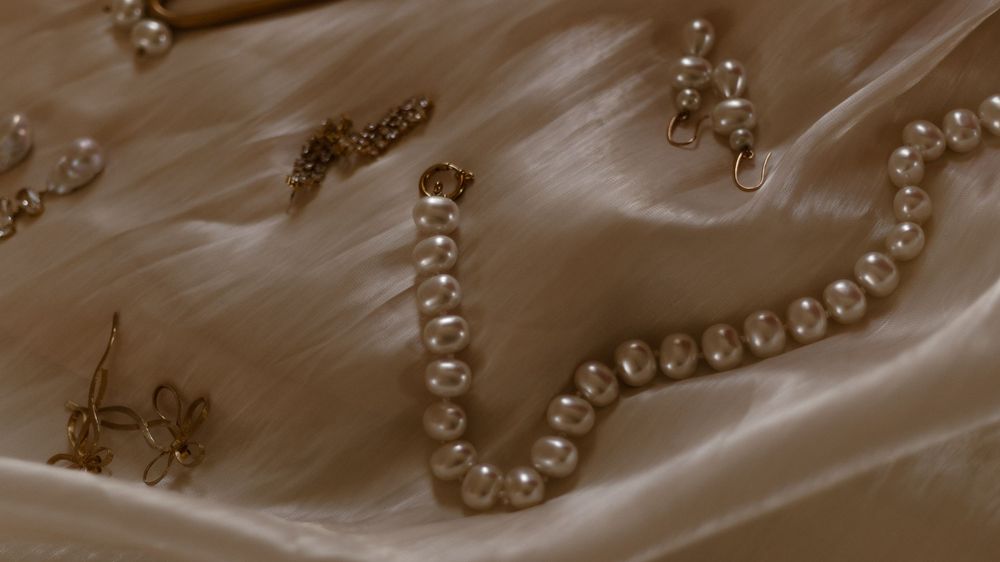 A close-up shot of pearl necklaces laying on light beige satin cloth with delicate folds and textures.