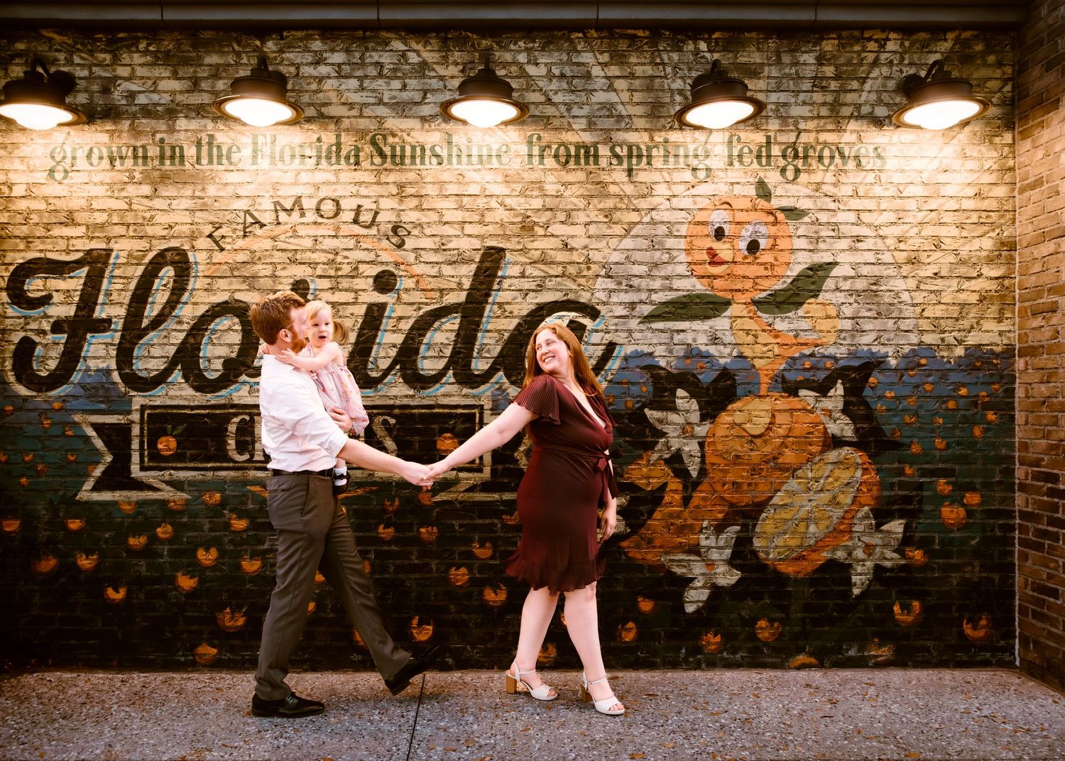 John & Emily anniversary photos at Disney Springs with baby Ripley, in front of the Florida Citrus Orange Bird Mural Cred: LexTakePix