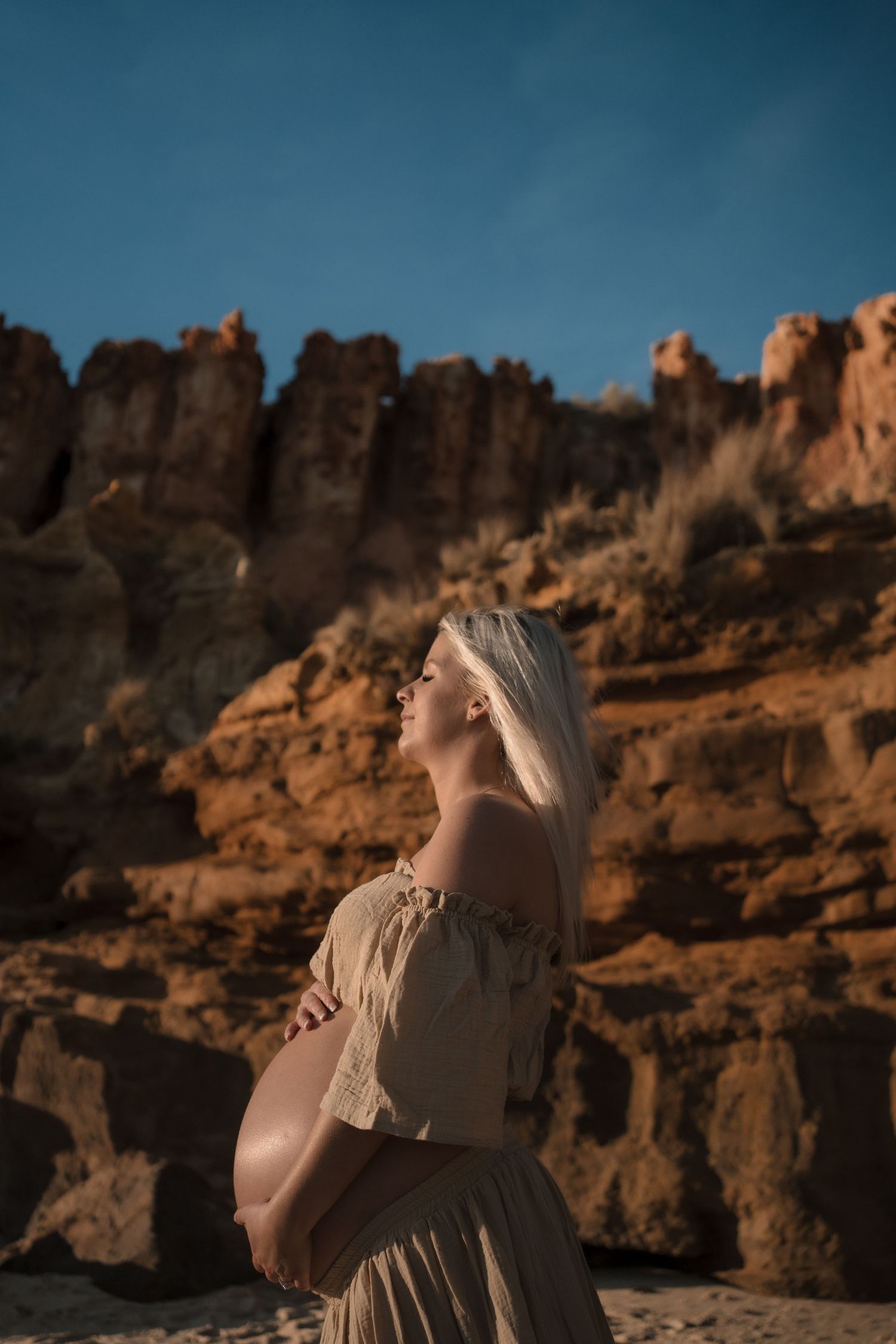 Woman in flowing dress poses dramatically against rugged beach rock formations at sunset at Half Moon Bay, Black Rock, Victoria
