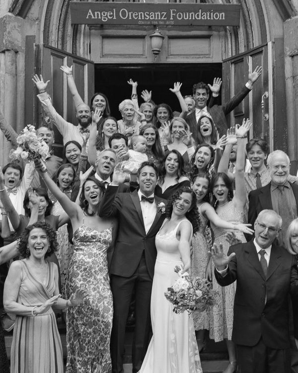 Jewish new york wedding party celebrating with raised arms outside a Angel Orensanz Foundation entrance in black and white photograph.