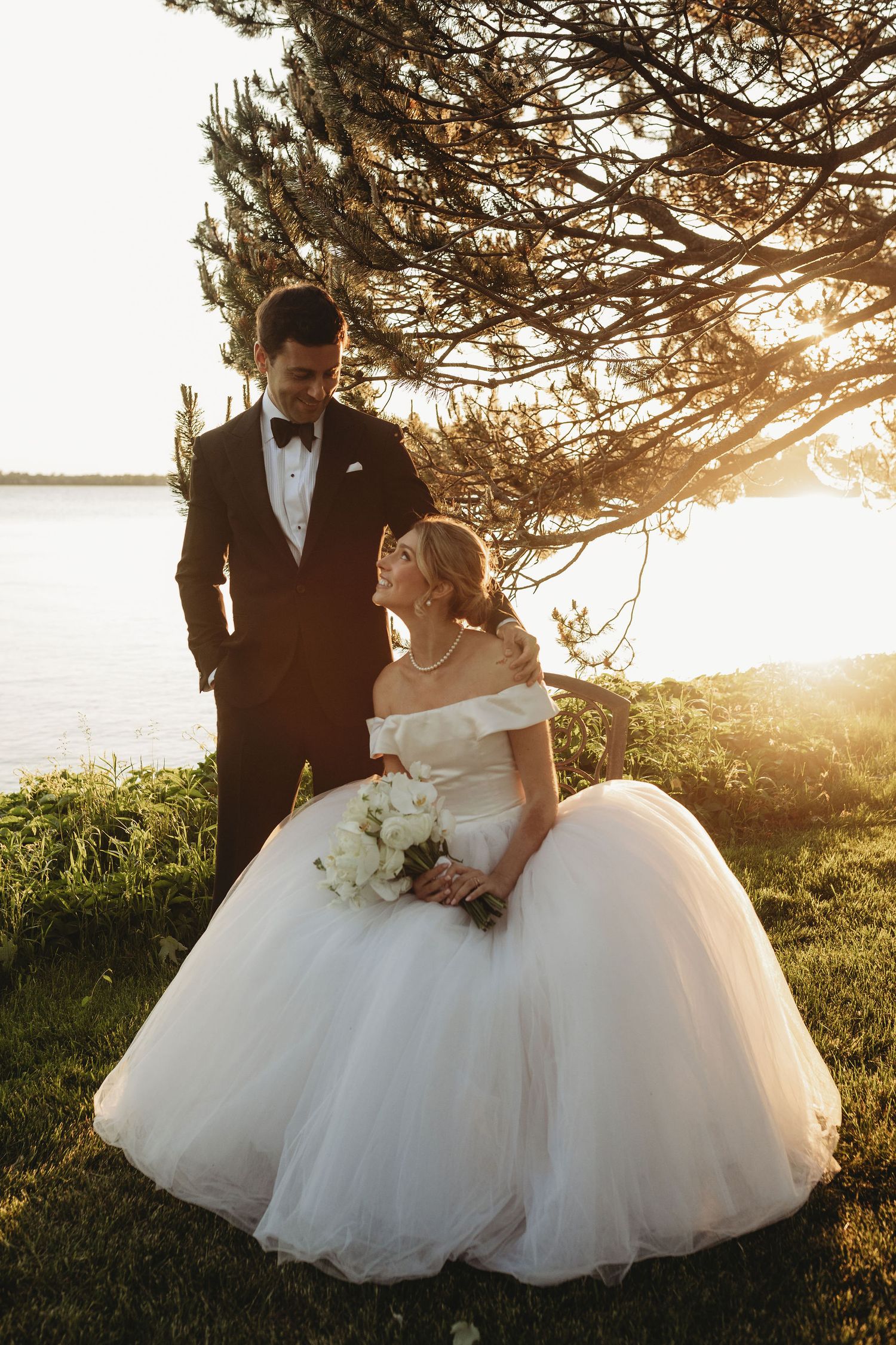 Romantic wedding couple embraces during golden hour sunset under pine trees in a natural outdoor setting.