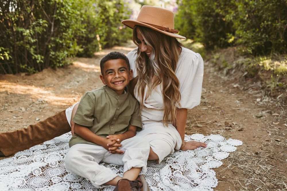 A couple sits together and laughs while enjoying time outdoors on a blanket on a sunny afternoon.