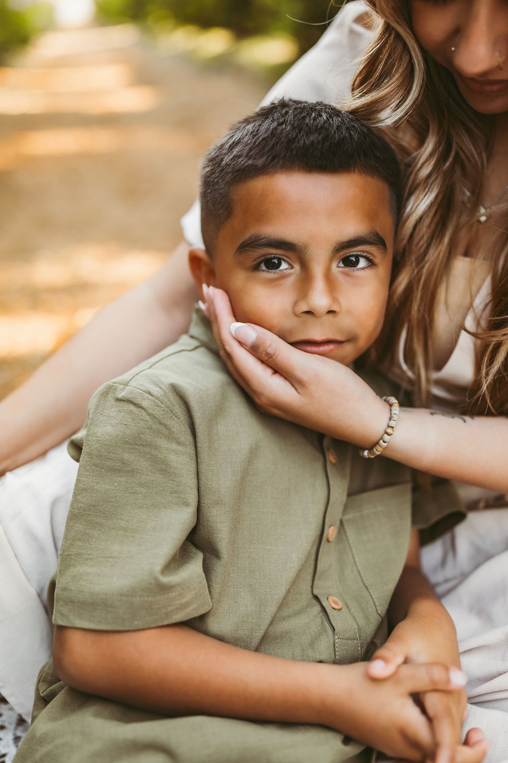 A tender moment captured in warm sunlight showing a child in a sage green shirt being embraced gently.