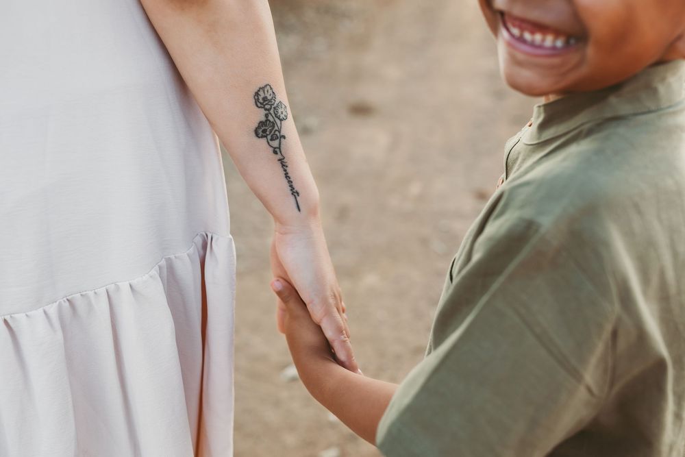 A close-up shot of a forearm with a simple rose tattoo and hands reaching out in connection.