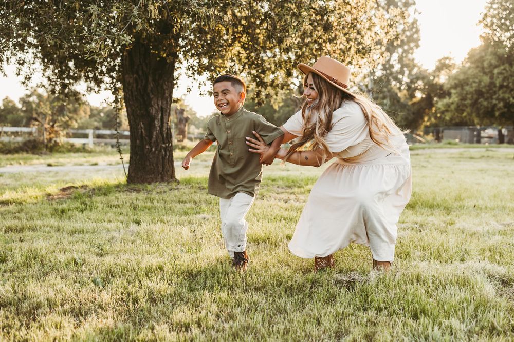 Two people in light summer clothing dance joyfully together in a sunlit grassy field at sunset.