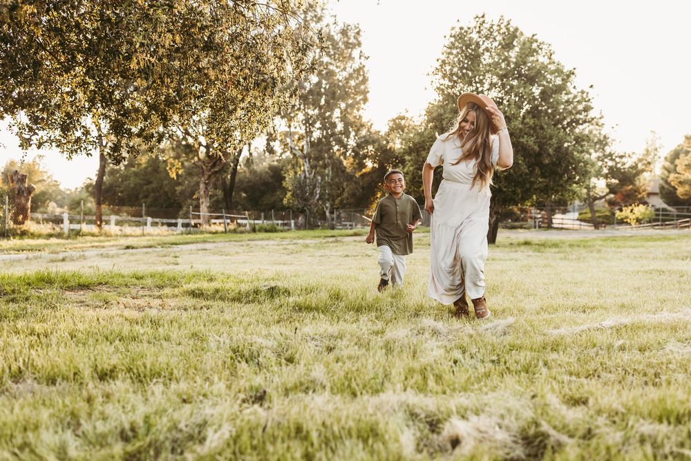 Two figures in white outfits share a tender moment walking together in a sun-drenched grassy field at golden hour.