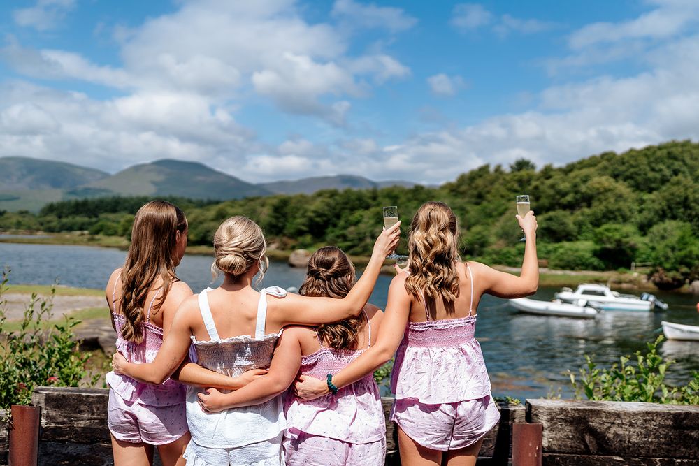 Group of friends in pink tops enjoying a scenic view of mountains and lake with boat in background.