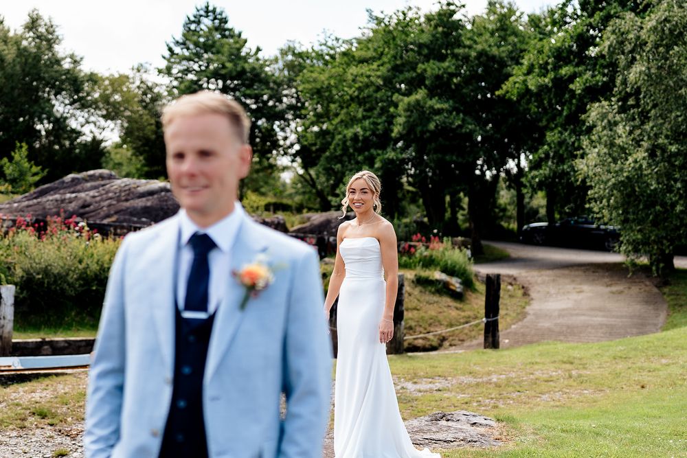 A wedding couple sharing their first look moment in a garden path surrounded by lush greenery.