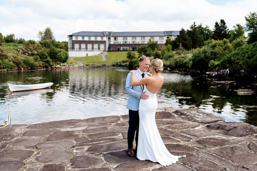 A romantic wedding moment captured on stone patio by a lake with a beautiful hotel building in the background.