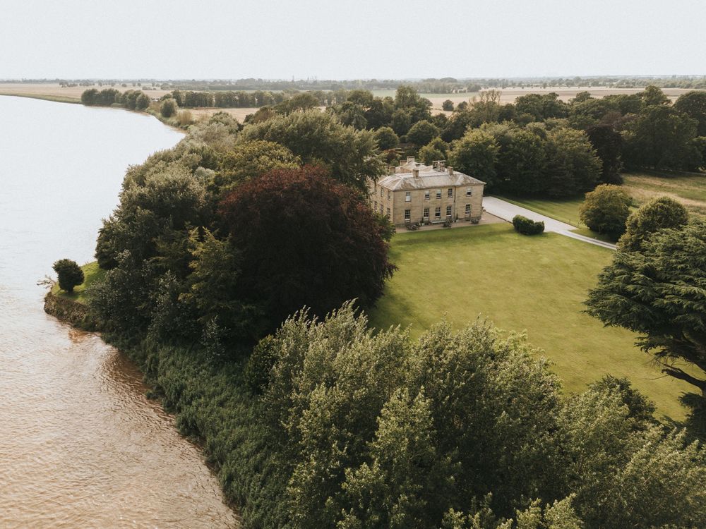 Mud-brown river snakes through lush green countryside with scattered trees and Saltmarshe Hall in the distance - by Grimsby photographer.