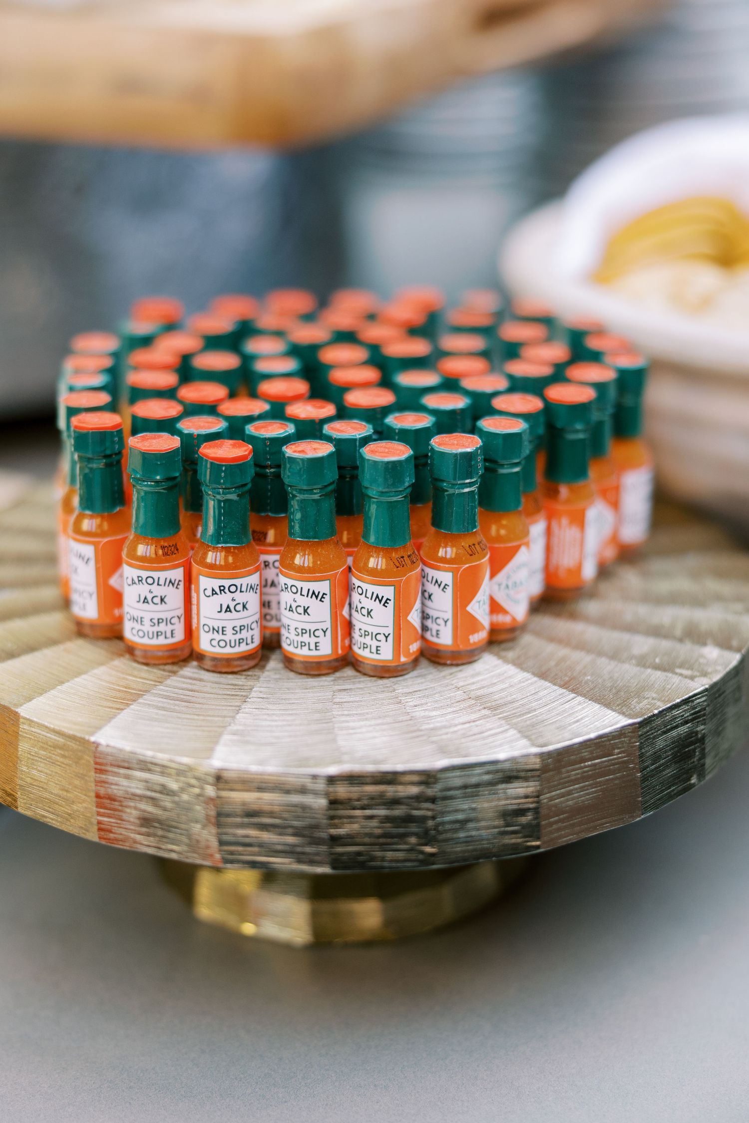 Small orange hot sauce favor bottles arranged in a circular pattern on a rustic wooden stand.