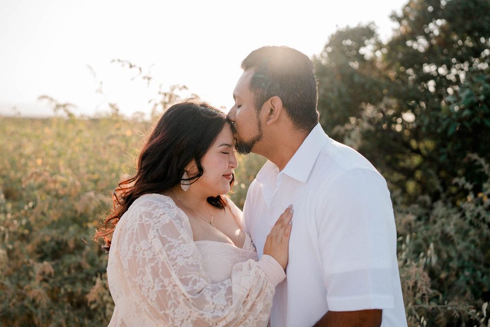 A romantic couple embraces and laughs together in a sunlit field at golden hour.