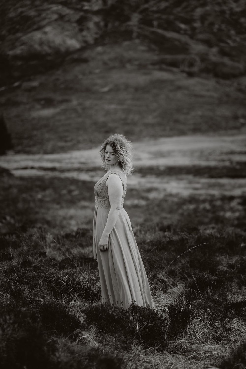Dramatic black and white portrait of a figure in a flowing dress standing on a misty hillside.