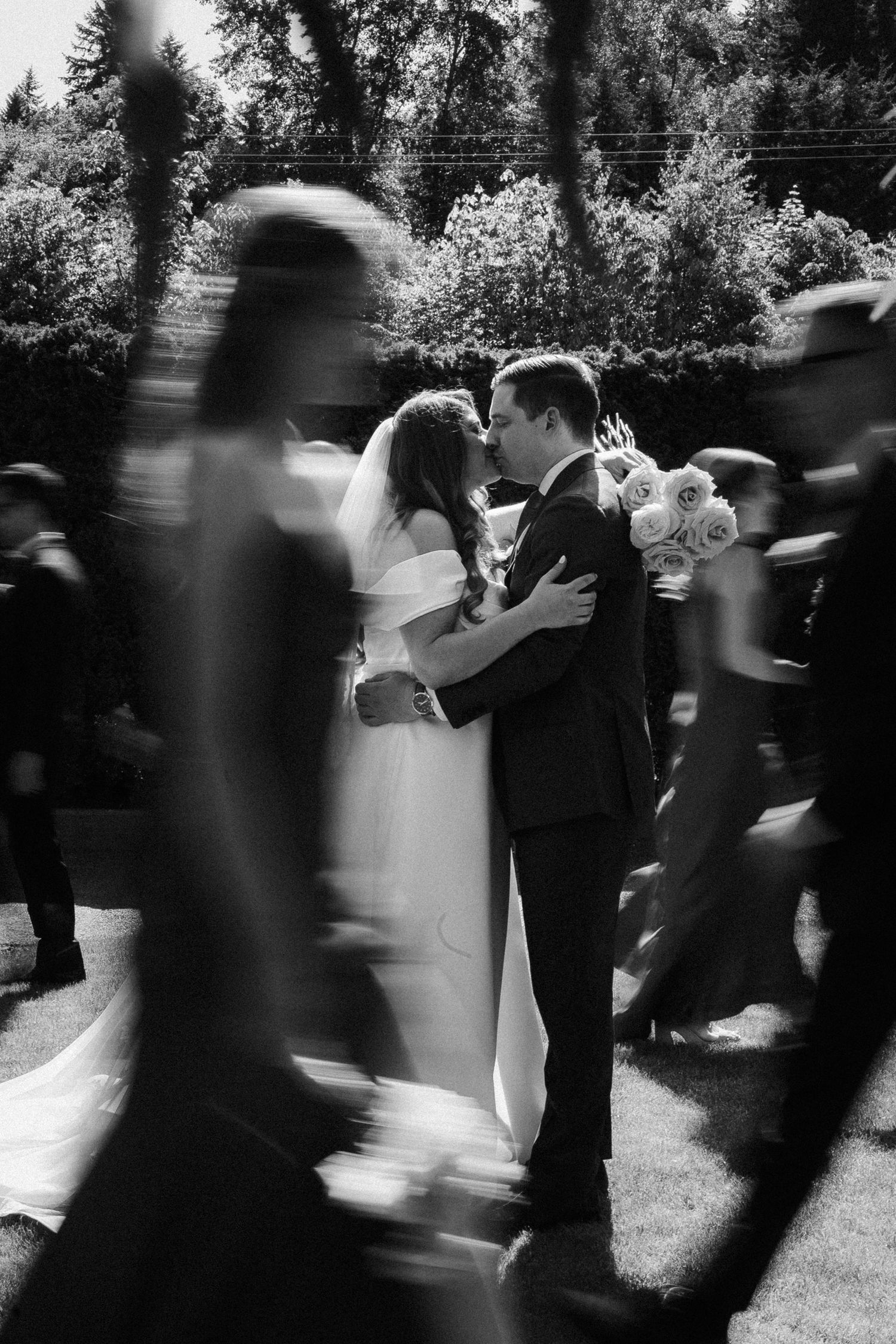 Black and white motion blur photograph of wedding guests dancing at an outdoor garden reception.