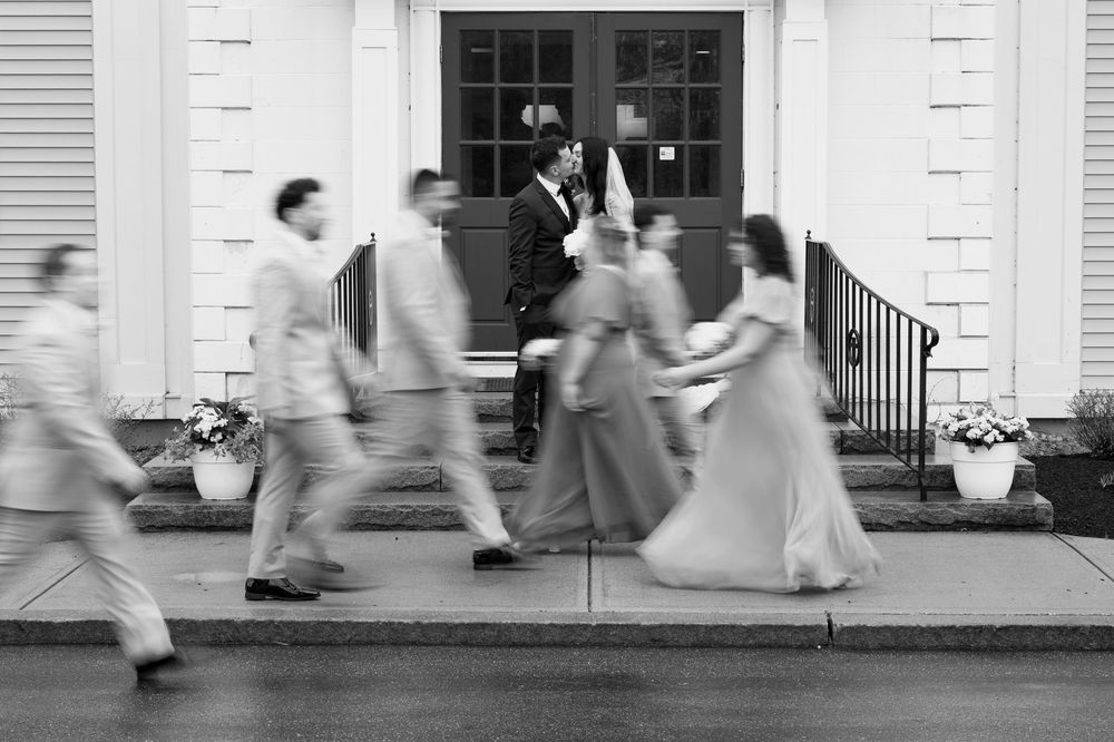 A motion-blurred black and white photograph shows people rushing past a white colonial-style building entrance.