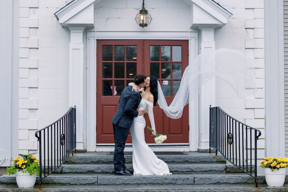 Elegant white church entrance with dual staircases and wedding couple silhouetted in doorway.