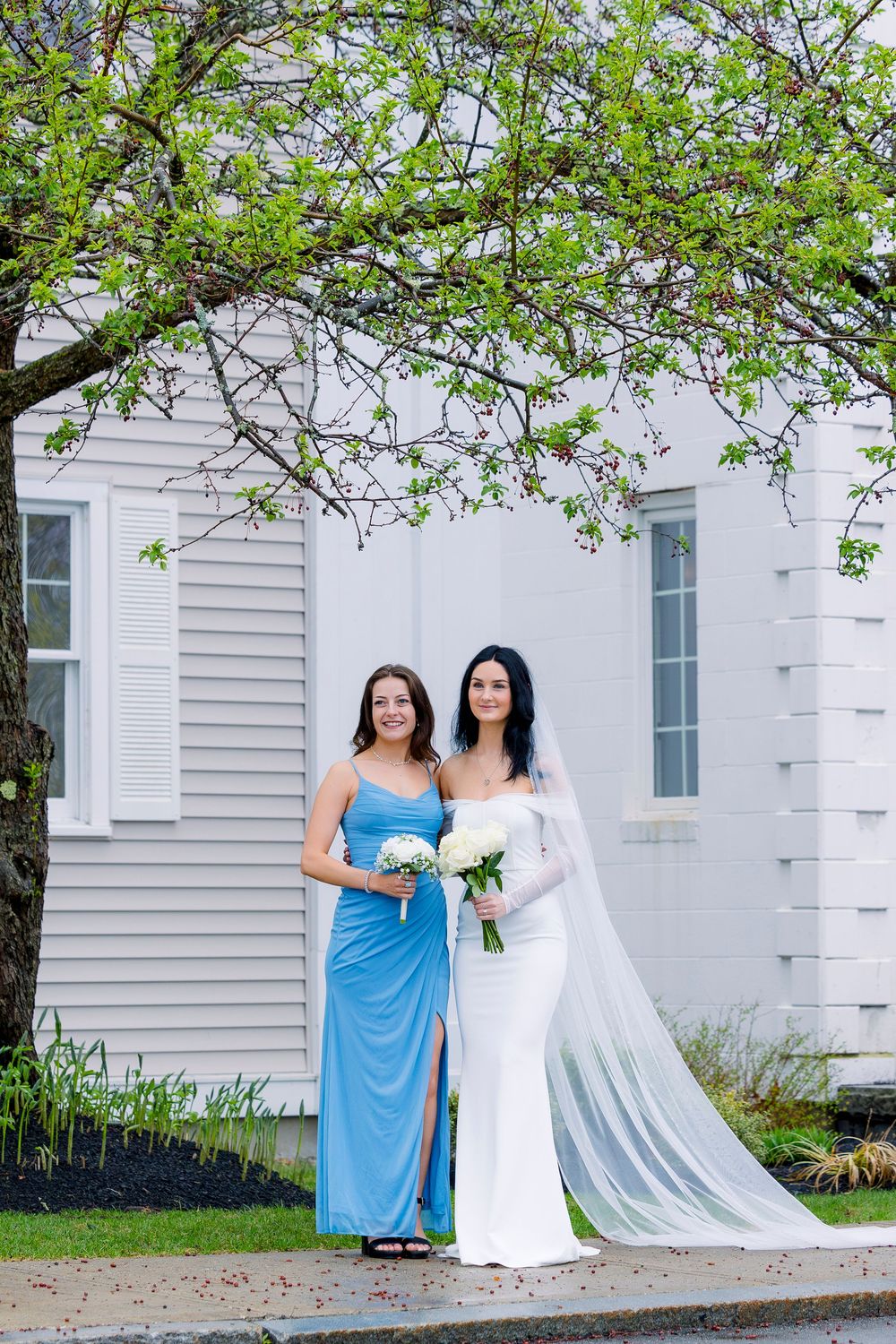 Outdoor wedding photography with bridesmaids in white and light blue dresses standing in front of a classic white church.