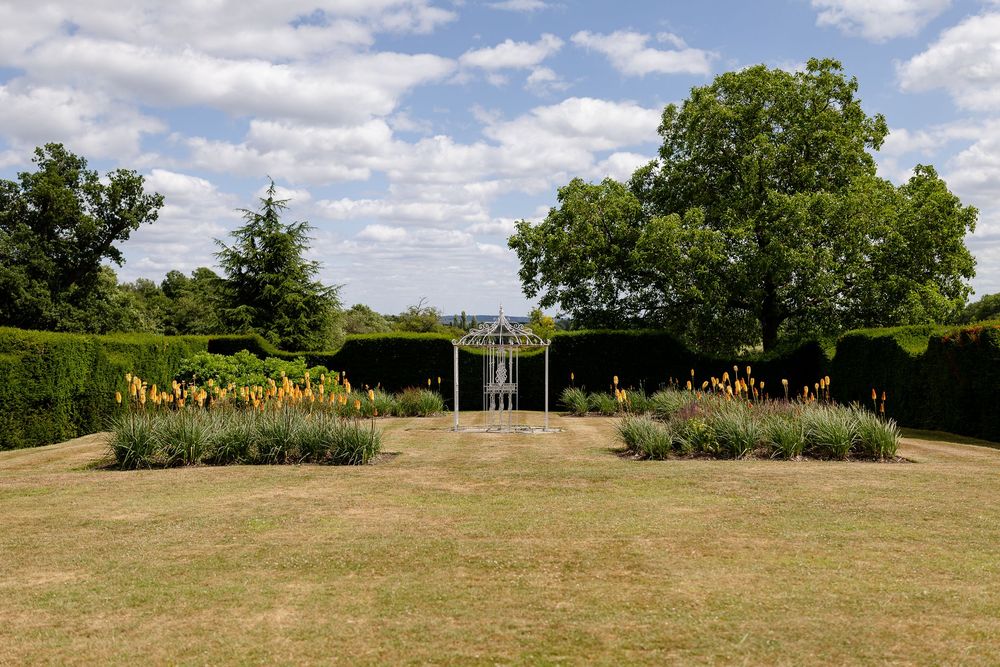 A panoramic view of a grassy meadow with wildflowers under puffy white clouds in a bright blue summer sky.