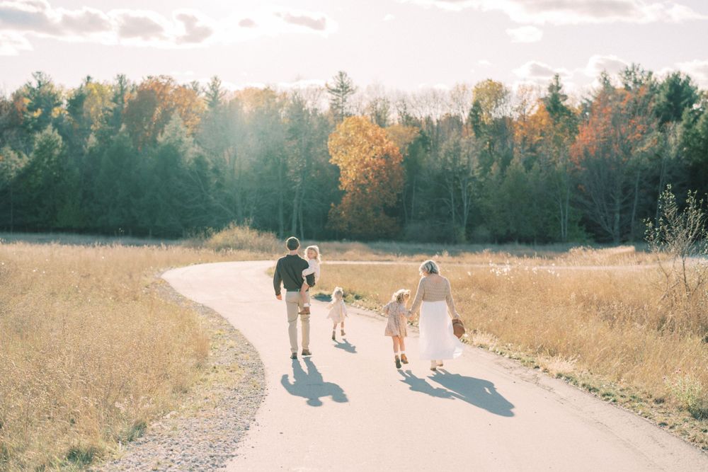 Family walking together on path through autumn meadow at sunset.