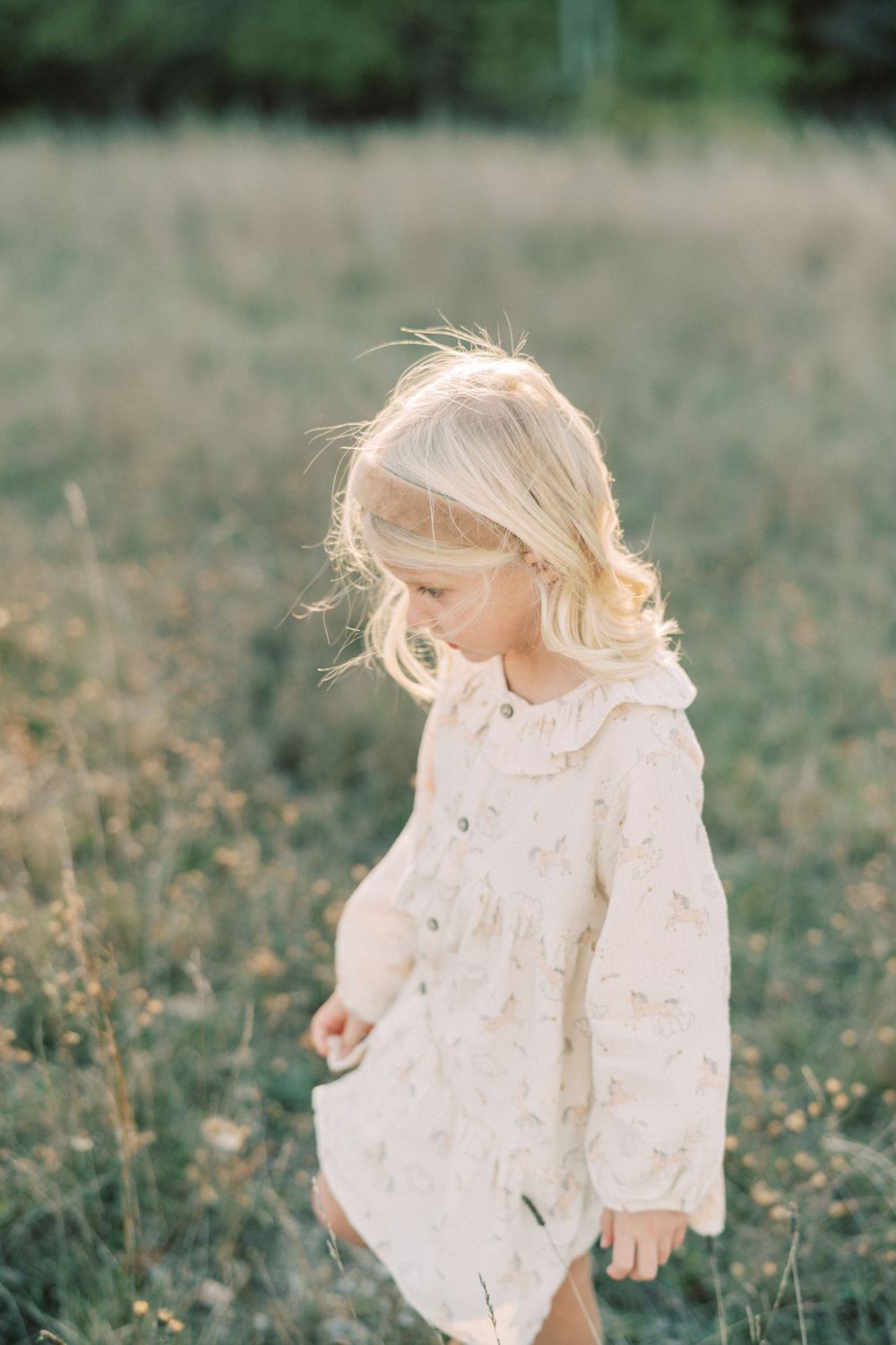 Child in white dress playing in autumn field with golden light.