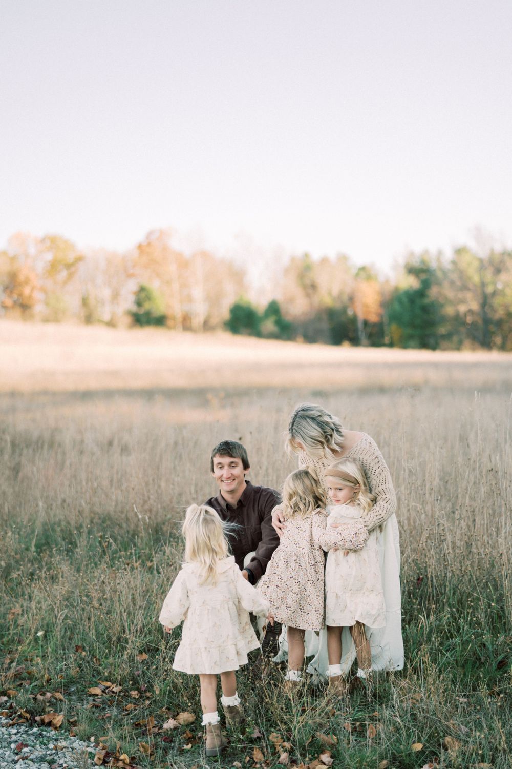 Family portrait in rustic field during golden hour wearing coordinated neutral colors.
