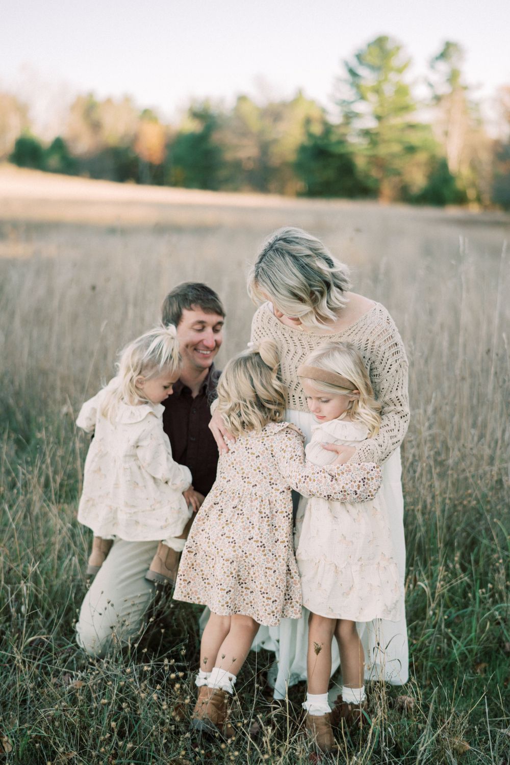 Candid family moment in autumn field wearing matching neutral toned outfits.
