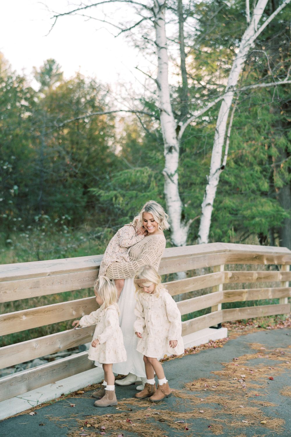 Mother and child share sweet moment while standing on wooden bridge deck with birch trees.