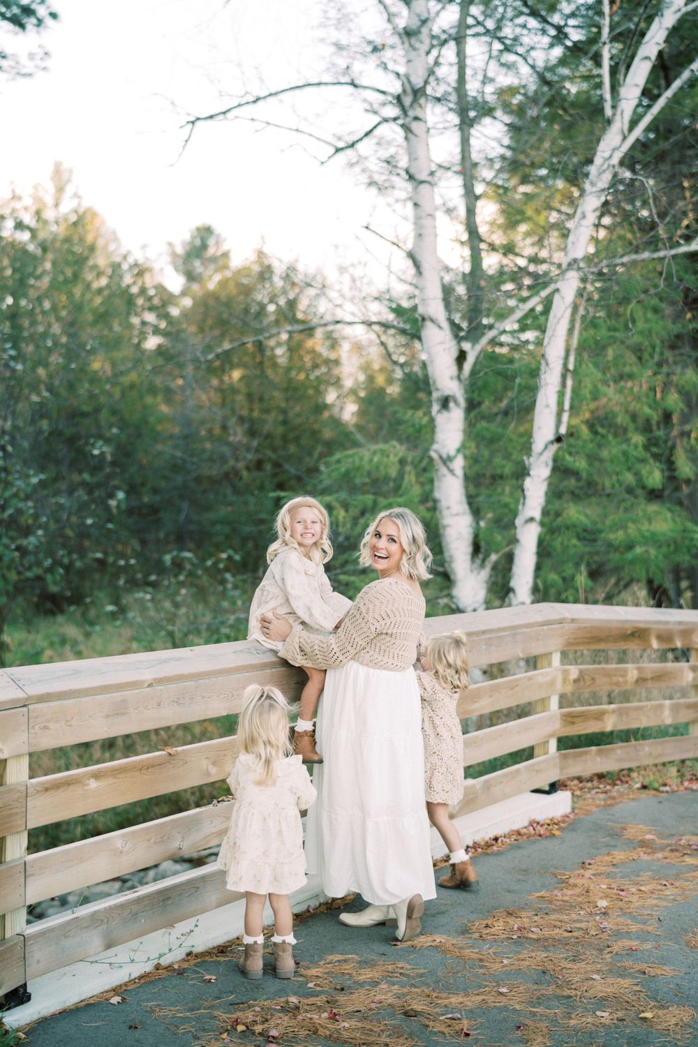 Family group poses together on wooden bridge walkway with white birch trees in background.