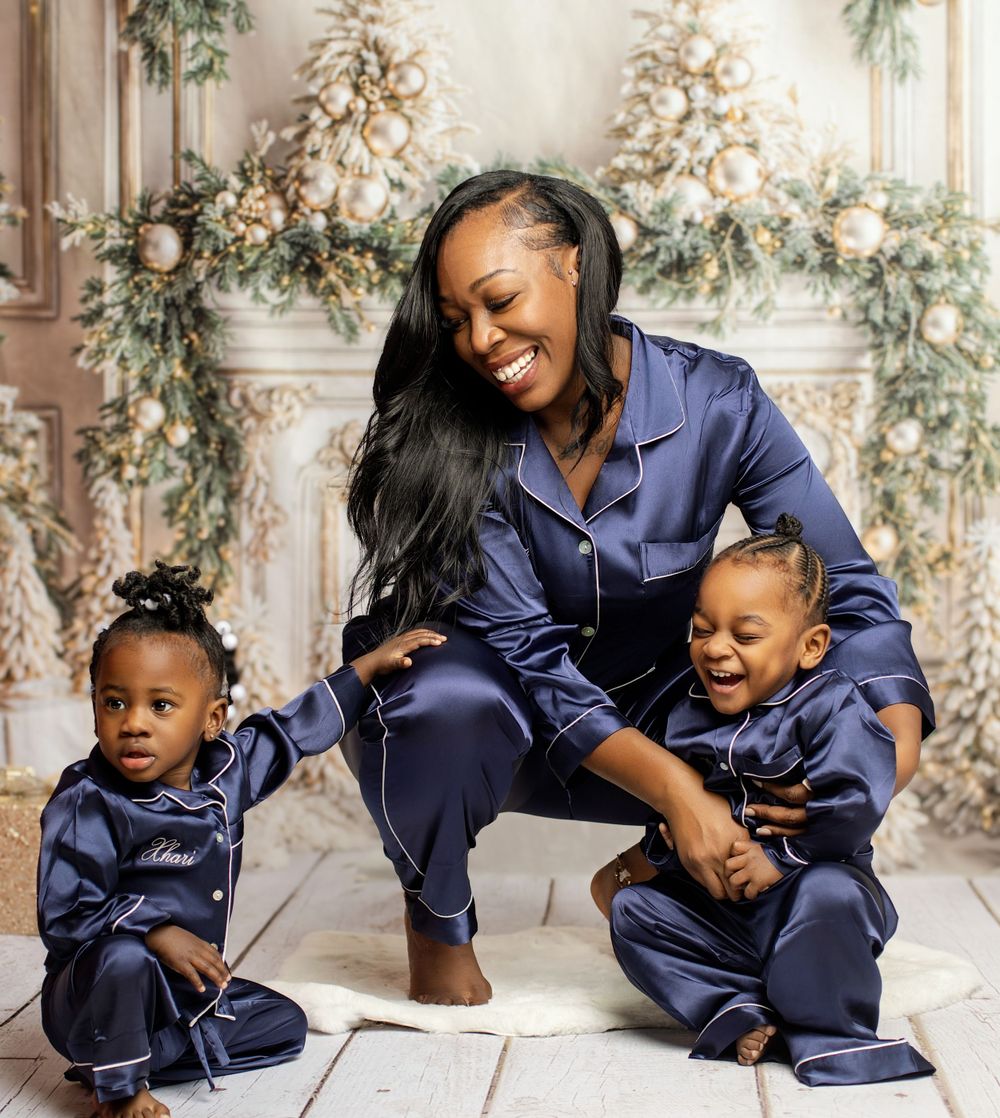 Coordinated family portrait in navy blue silk pajamas against elegant Christmas backdrop.