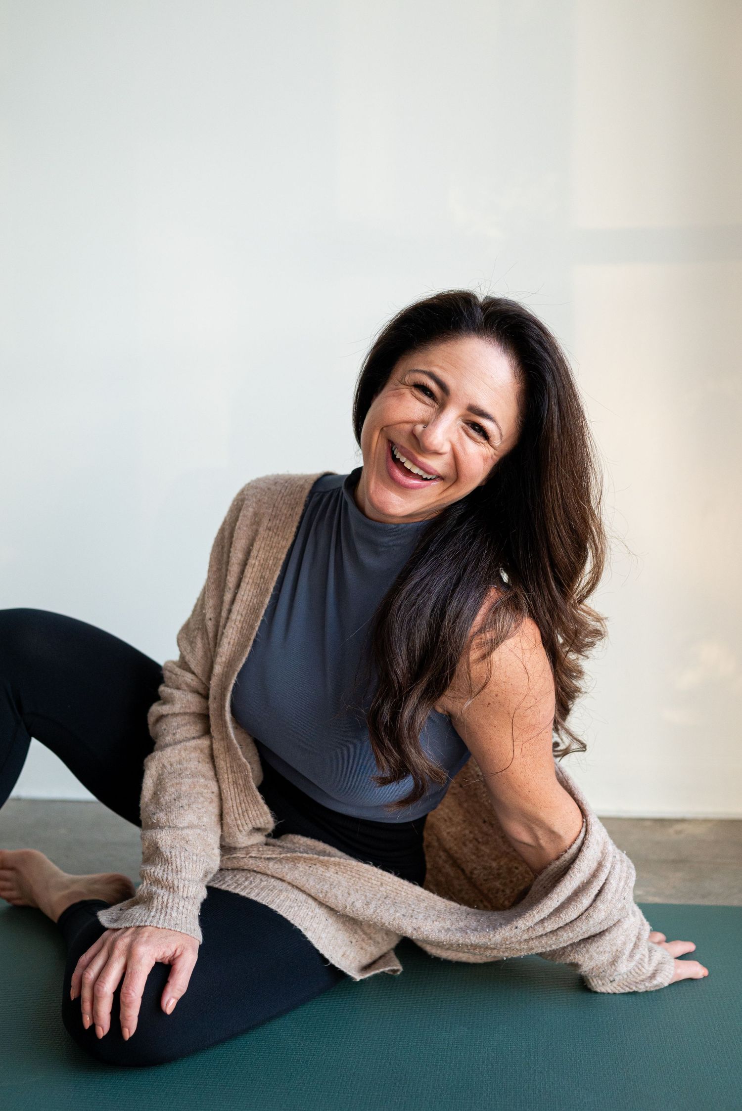 Person relaxing on yoga mat wearing gray tank top and beige cardigan.
