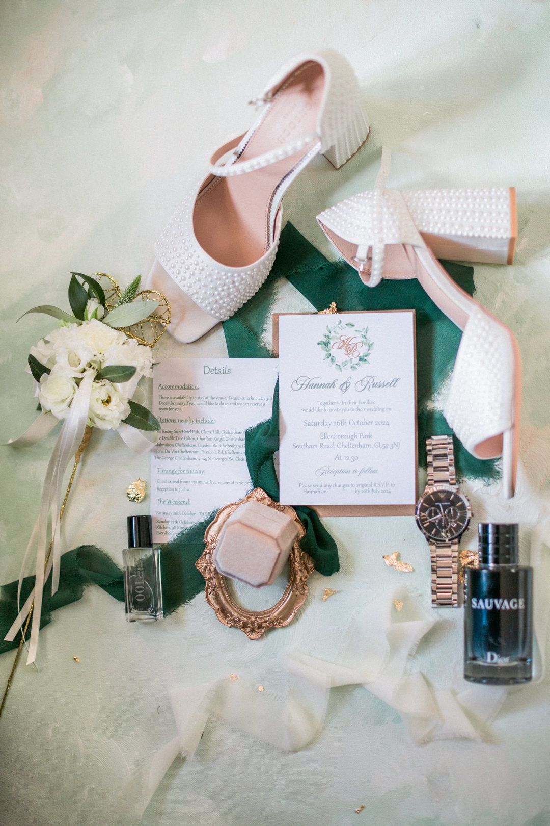Wedding details flatlay with pearl shoes, stationery, watch, perfume bottles and white flowers on emerald green velvet at ellenborough park