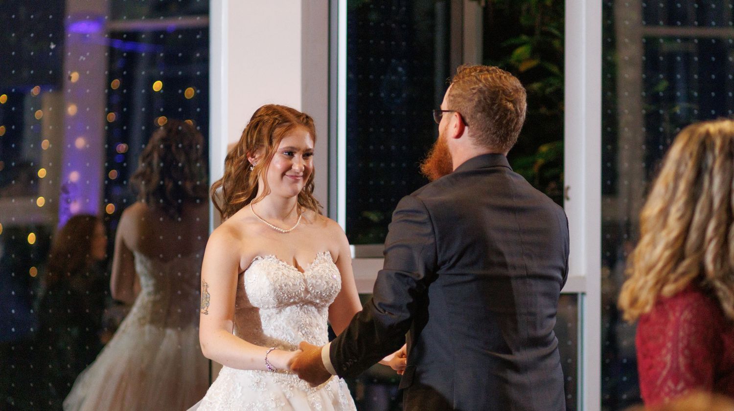 Wedding guests dance and celebrate during an evening reception in an elegant venue with colorful lighting.